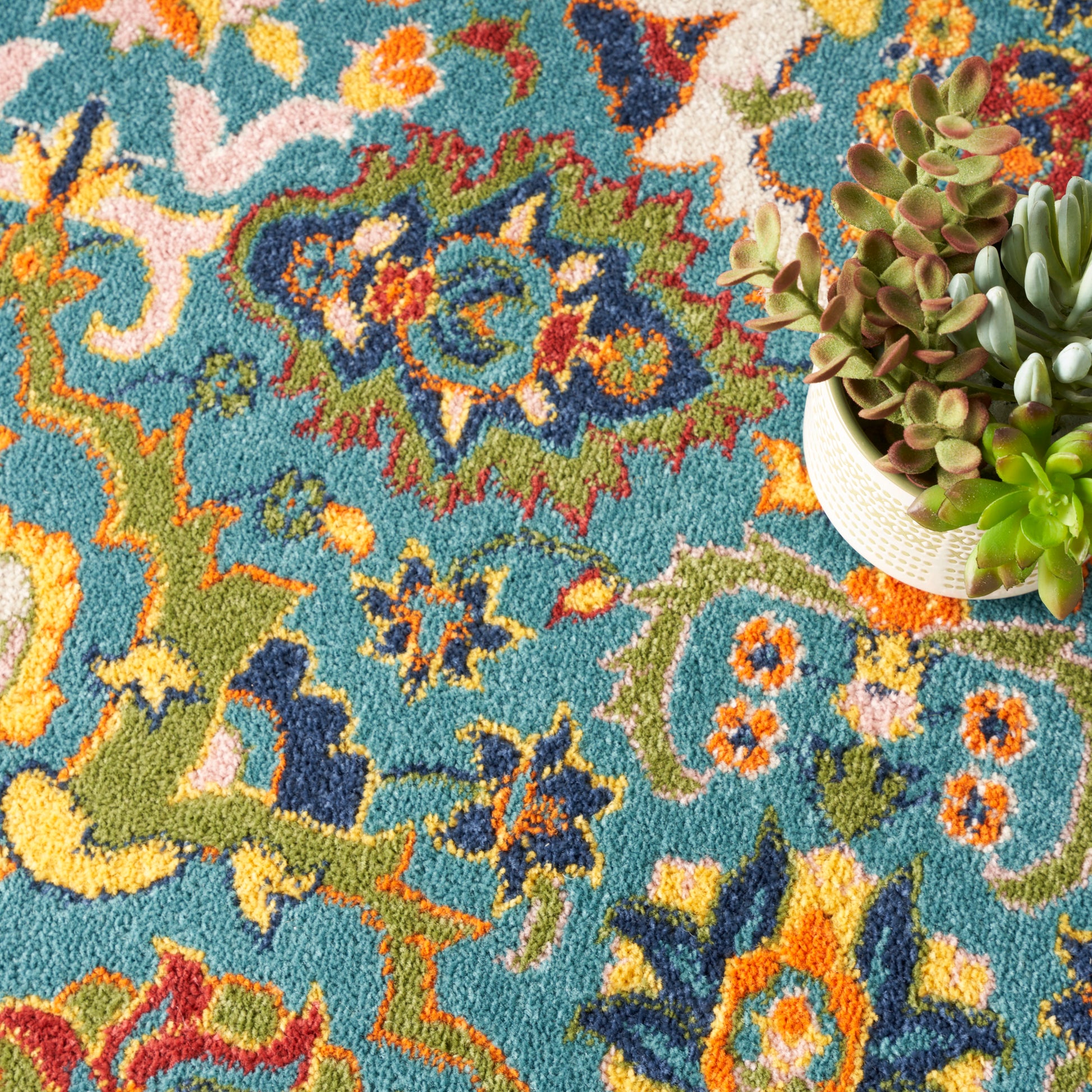Vibrant teal rug with multicolor oriental pattern in orange, yellow, green, blue; succulent plant in beige pot on the right