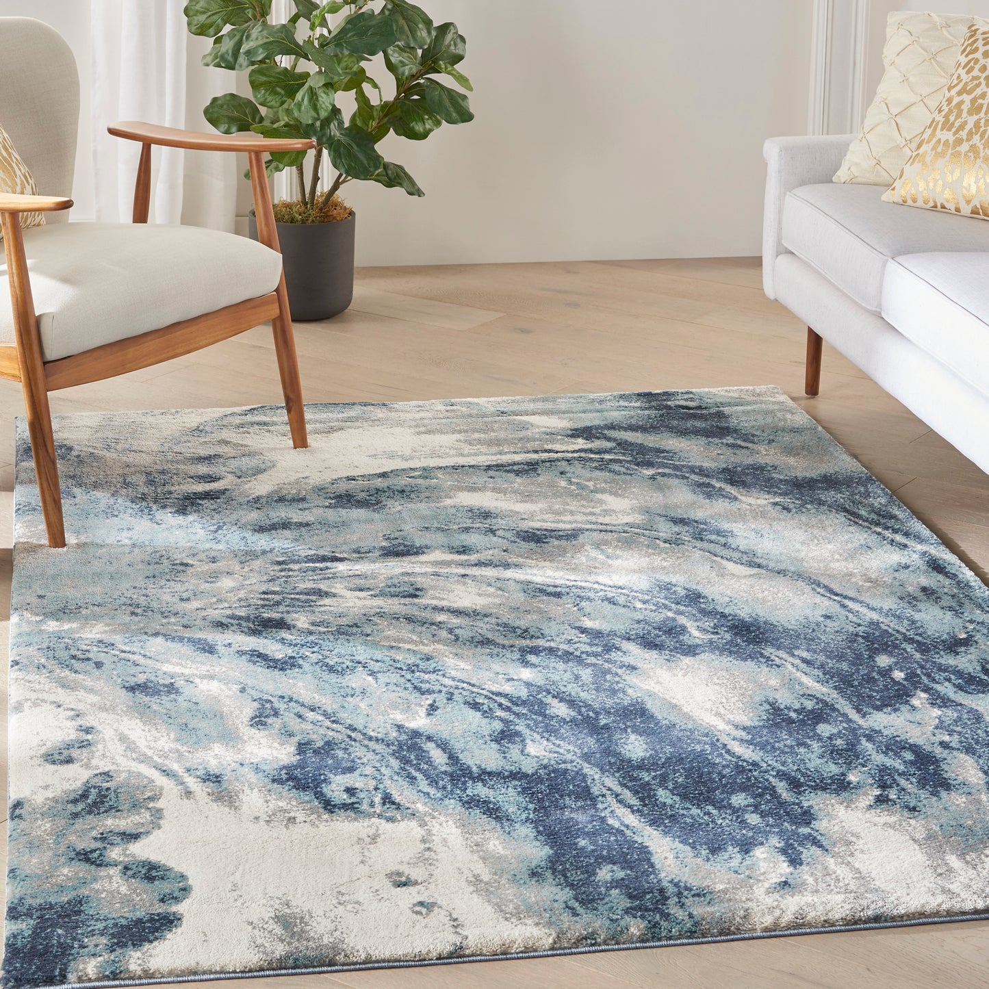 Blue and white abstract rectangular rug on light wood floor in a modern living room with a wooden-framed chair and white sofa.