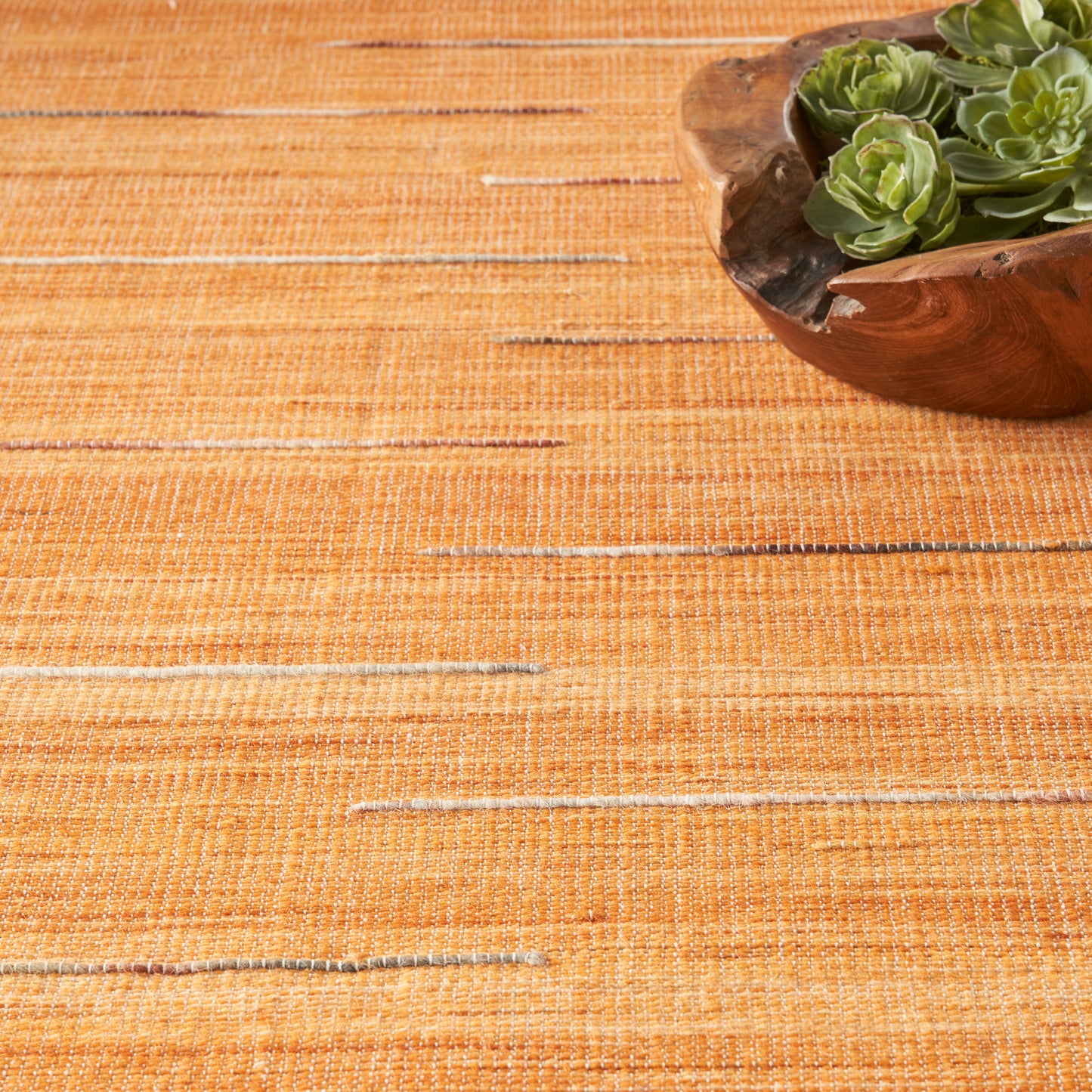 Orange woven placemat with a wooden bowl holding green succulents in the top-right corner.