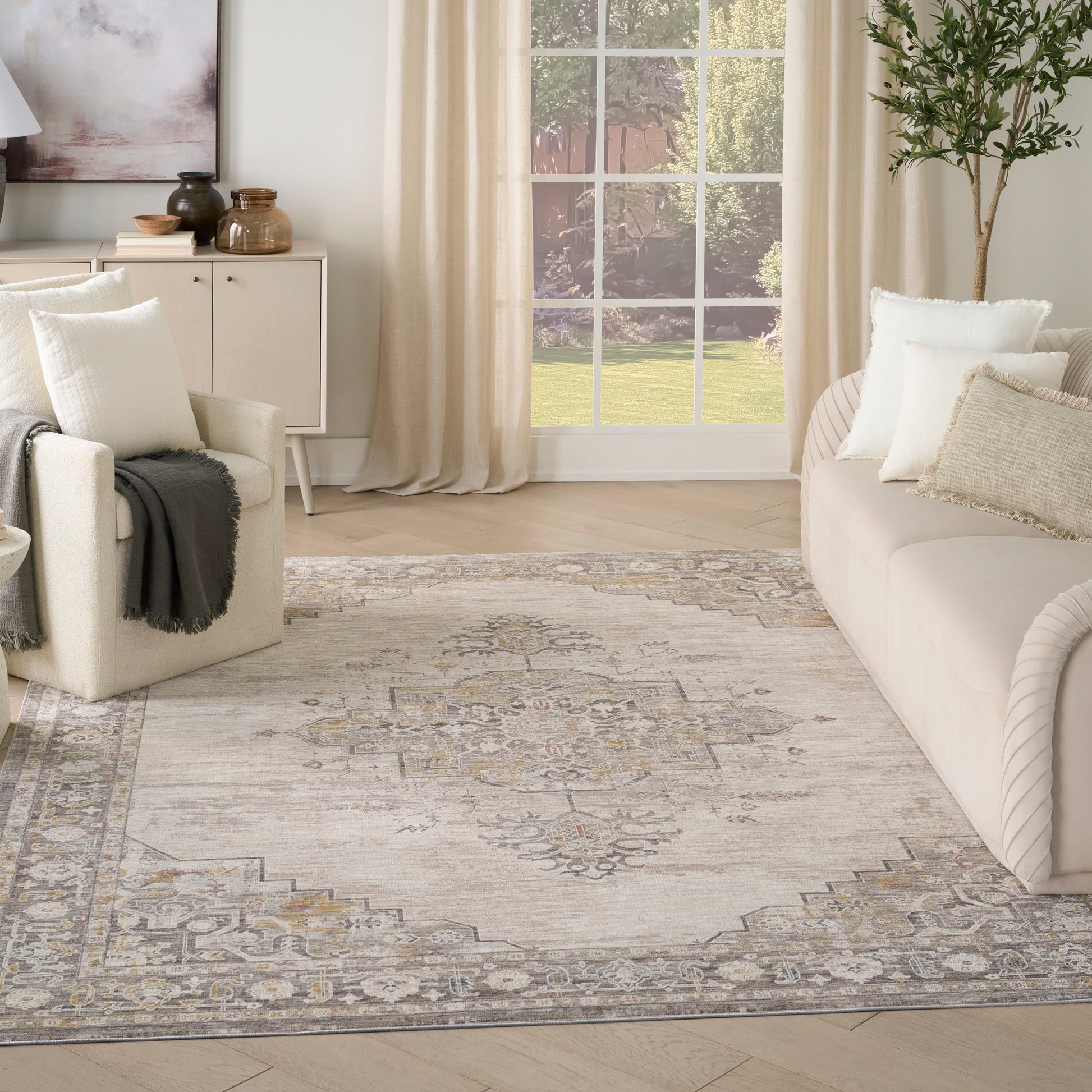 Neutral living room with an ornate beige-gray area rug, cream sofa, white armchair, and beige-curtained window.