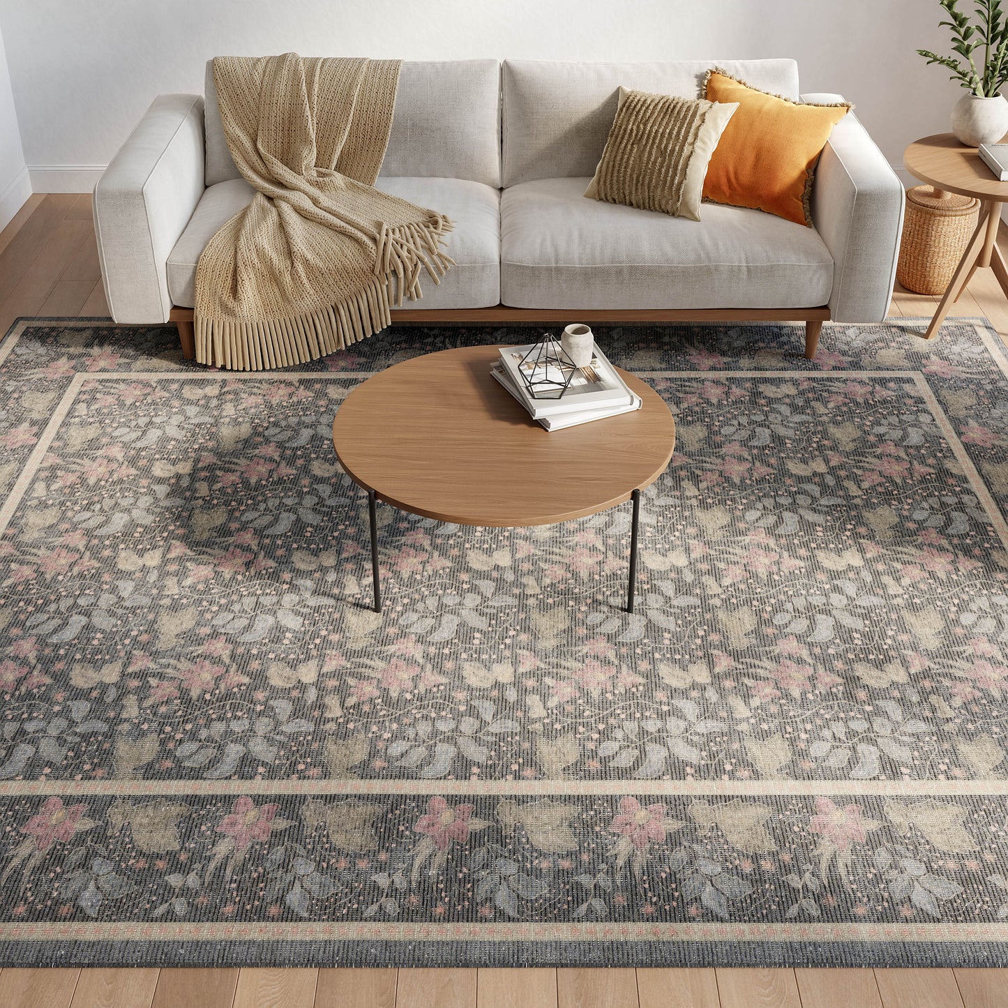 Light gray sofa with beige throw and orange pillow, round wood coffee table on a vintage floral rug in a modern living room.