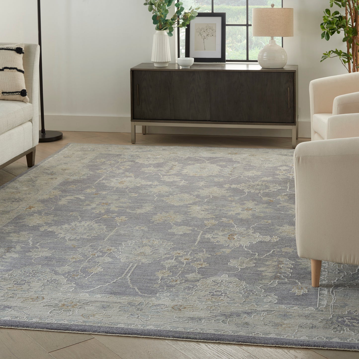 Cozy living room with a blue-gray patterned area rug, beige seating, and a dark wood console under a bright window.