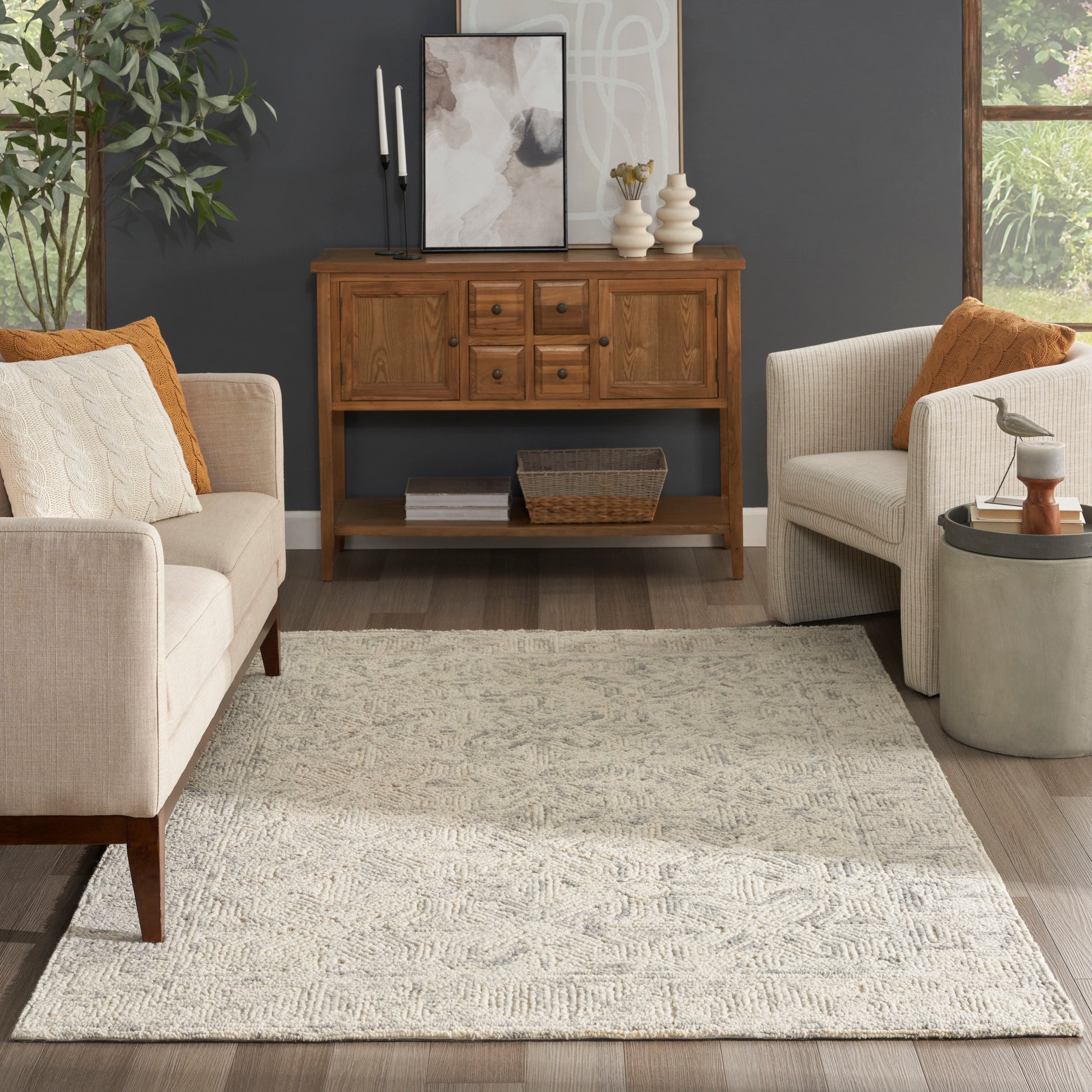 Beige mid-century living room with warm wood sideboard against a dark wall, cream textured rug, and neutral fabric chairs.