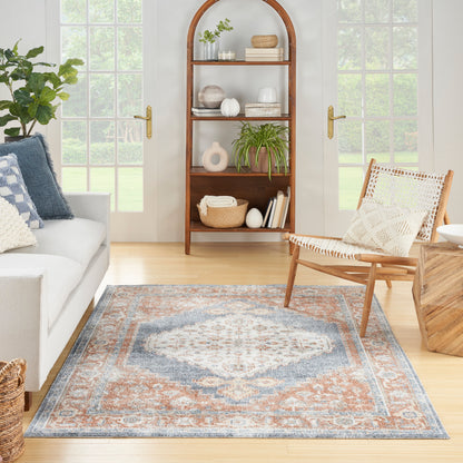 Vintage 4' x 6' blue and orange patterned rug in a sunlit living room with a light gray sofa and plants.