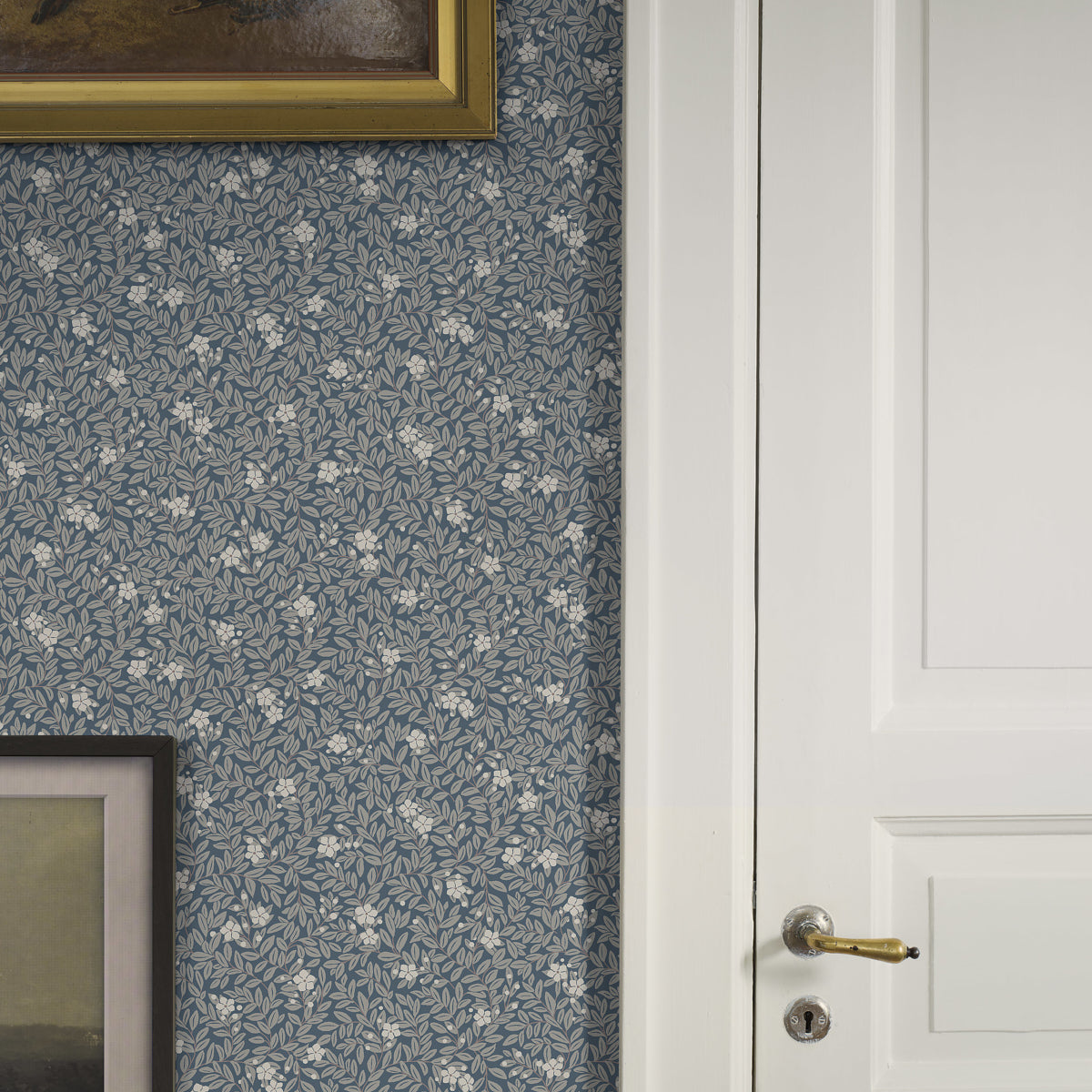 Blue floral wallpaper with small leaf pattern, white paneled door with brass handle, gold-framed artwork edges visible.