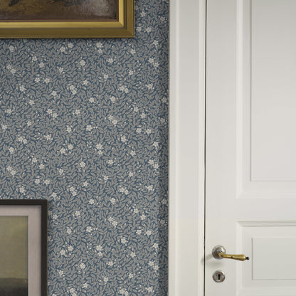 Blue floral wallpaper with small leaf pattern, white paneled door with brass handle, gold-framed artwork edges visible.