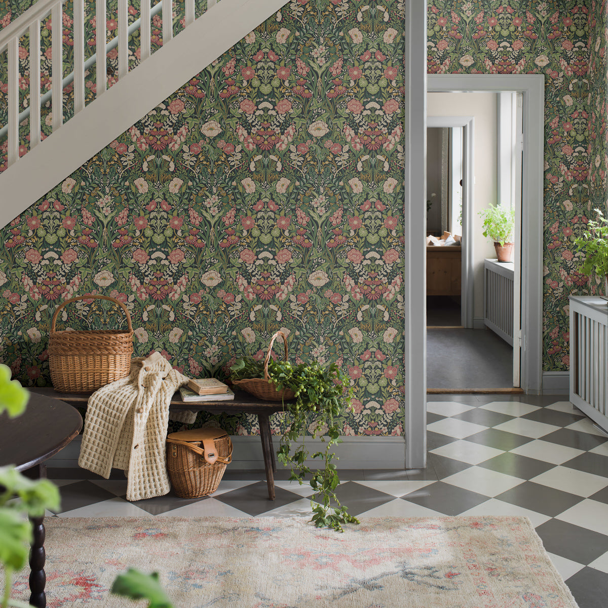 Entry hall with dark green floral wallpaper, white staircase, gray-and-white floor tiles, bench with baskets and knit throw.