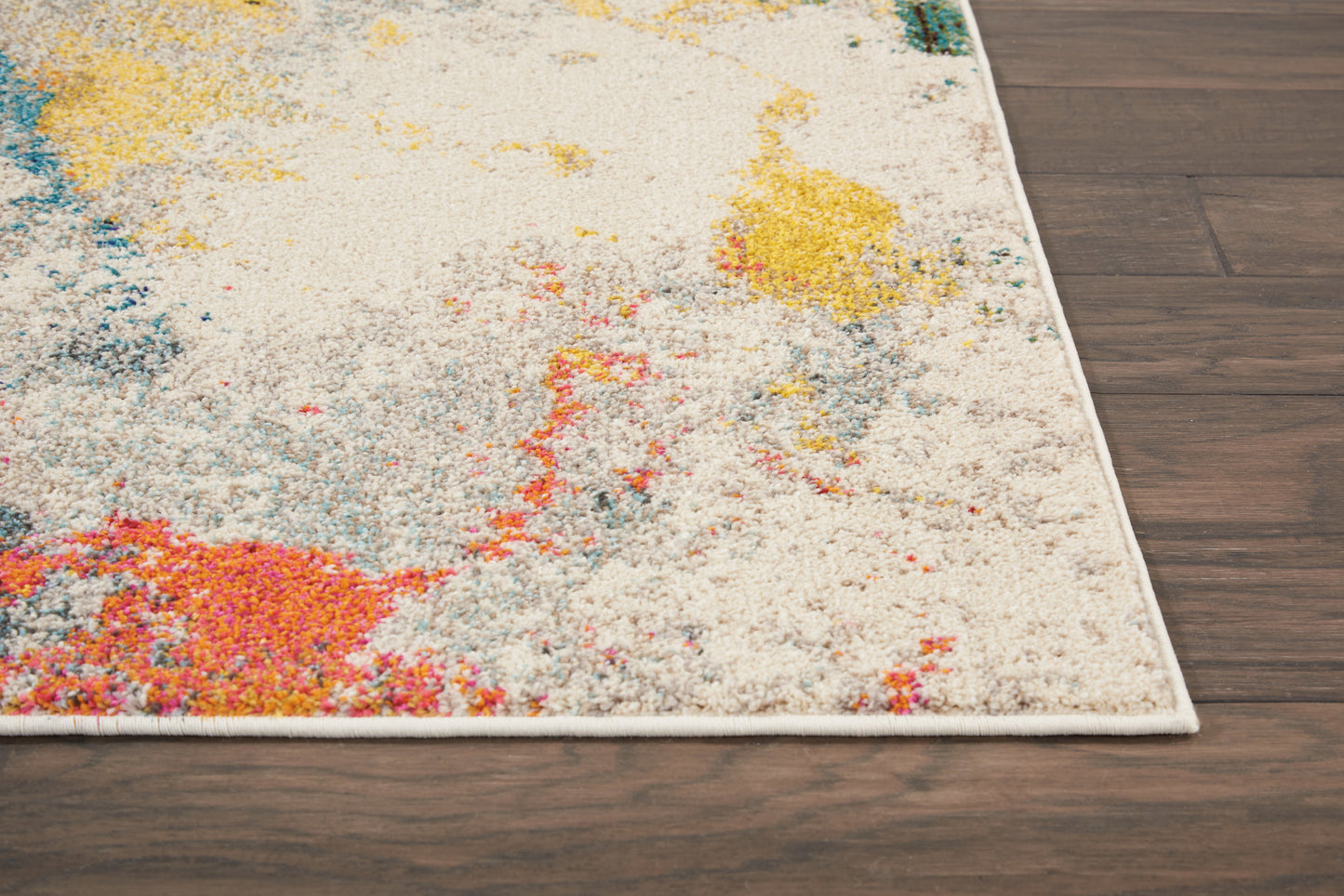 Colorful abstract area rug with cream base and vibrant pink, yellow, blue and orange splashes, white fringe, on dark wood floor.