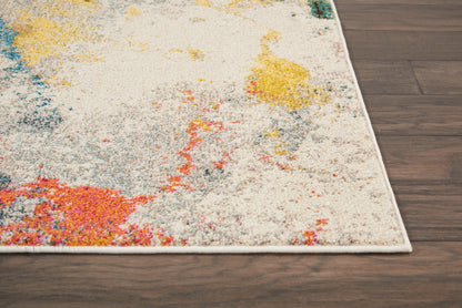 Colorful abstract area rug with cream base and vibrant pink, yellow, blue and orange splashes, white fringe, on dark wood floor.