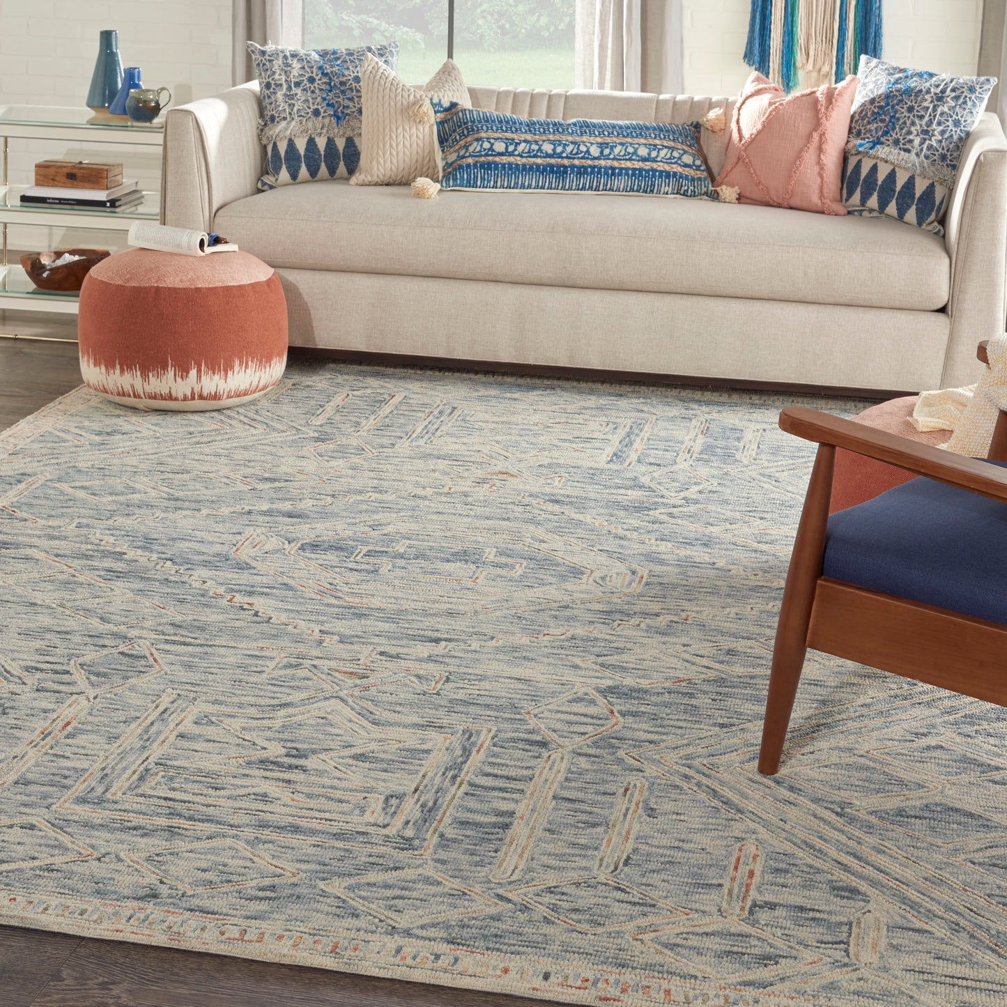 Cozy living room with beige sofa, blue patterned cushions, round pink pouf, and blue geometric area rug.