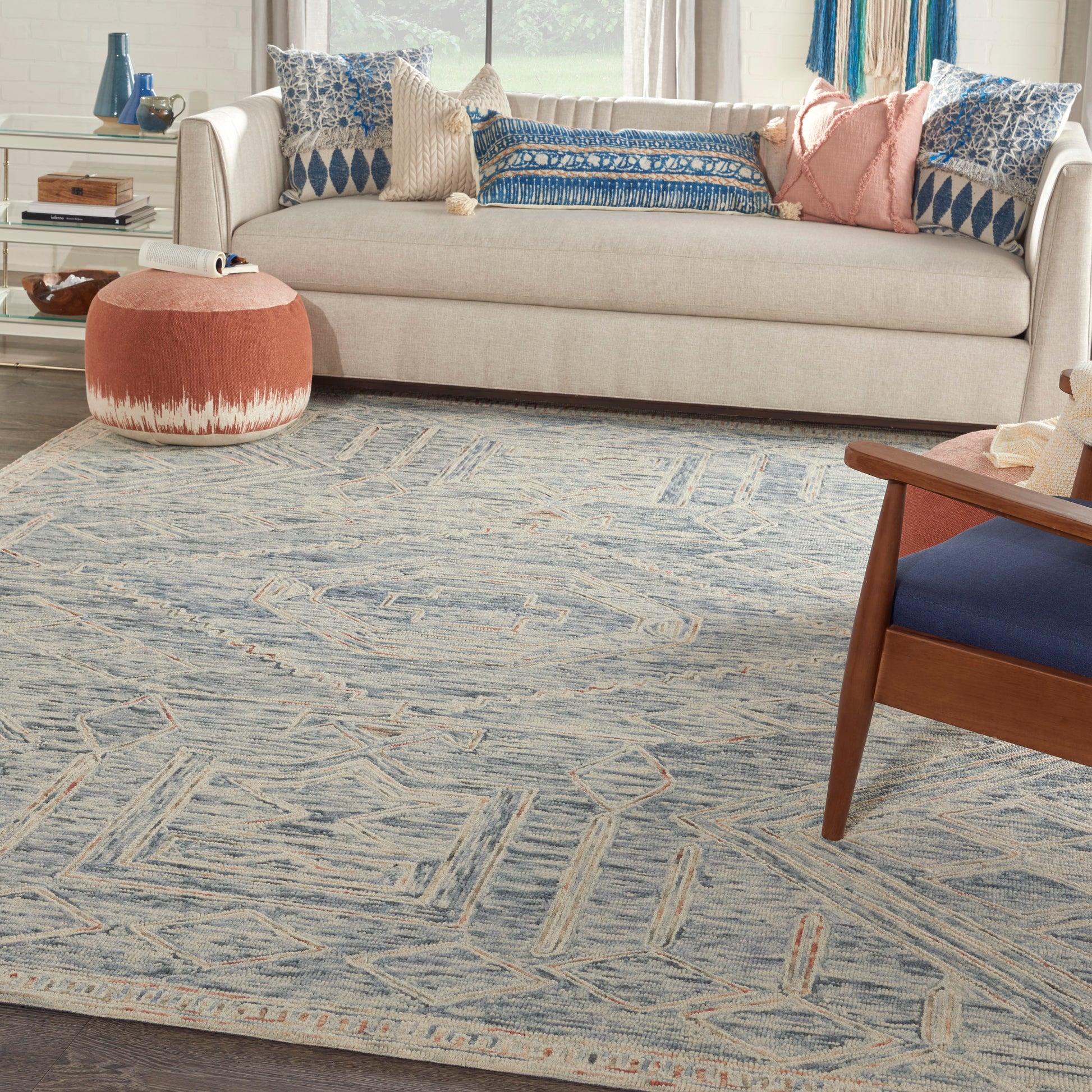 Cozy living room with beige sofa, blue patterned cushions, round pink pouf, and blue geometric area rug.