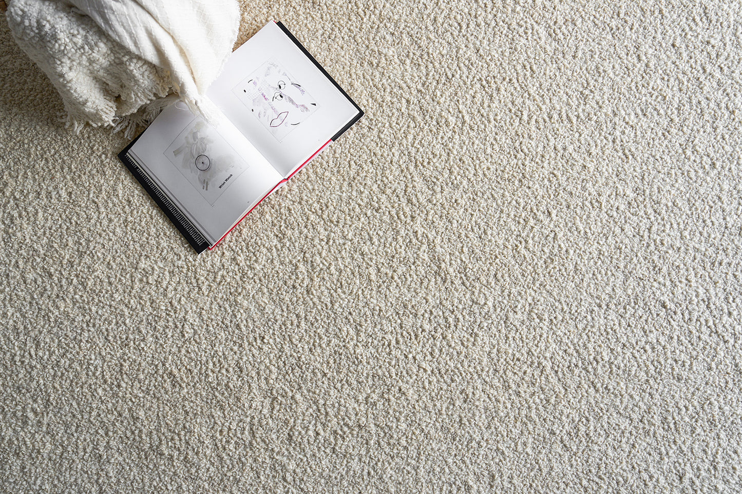 Beige shaggy rug with an open illustrated book and a white fluffy throw blanket for a cozy reading setup.