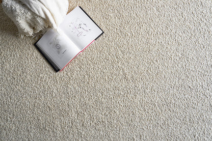 Beige shaggy rug with an open illustrated book and a white fluffy throw blanket for a cozy reading setup.