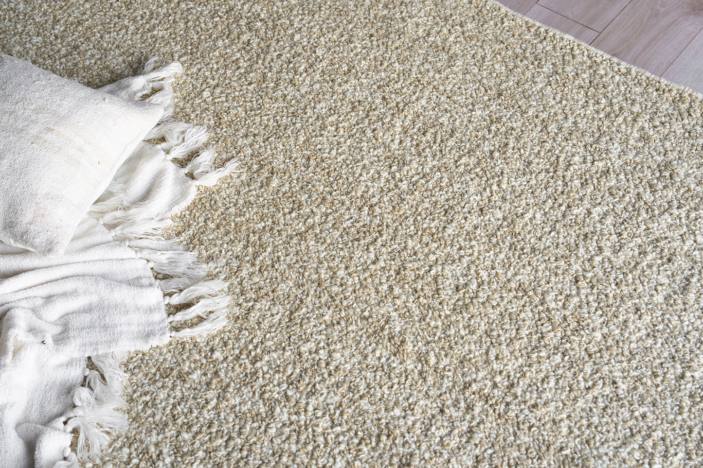 Beige shag rug with dense loop texture and fringe, paired with a white throw blanket and pillow.