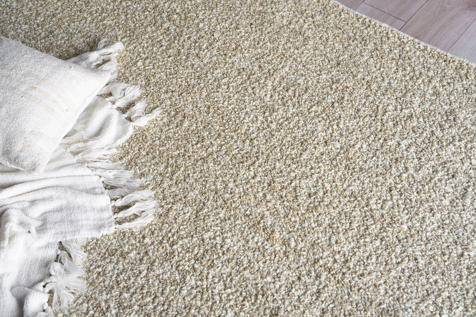 Beige shag rug with dense loop texture and fringe, paired with a white throw blanket and pillow.
