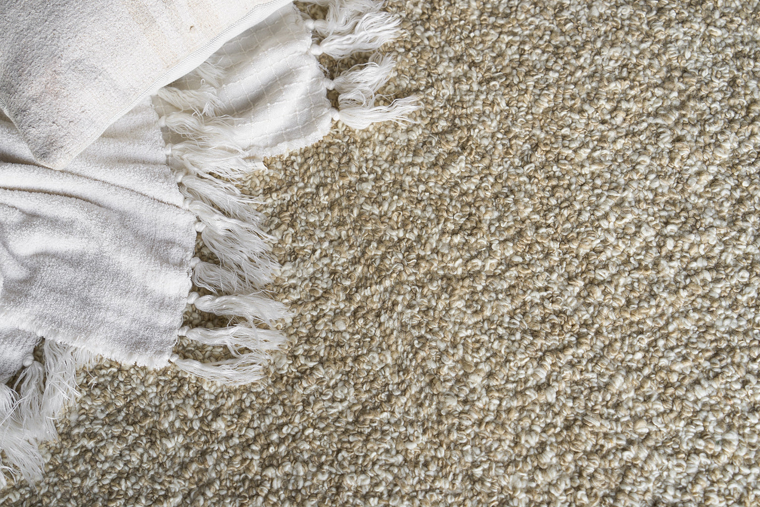 Beige shag rug with white fringe along the edge and a white textured throw draped on the corner.