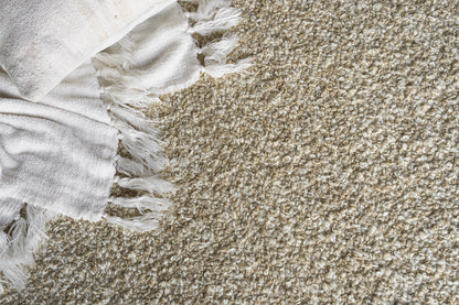 Beige shag rug with white fringe along the edge and a white textured throw draped on the corner.