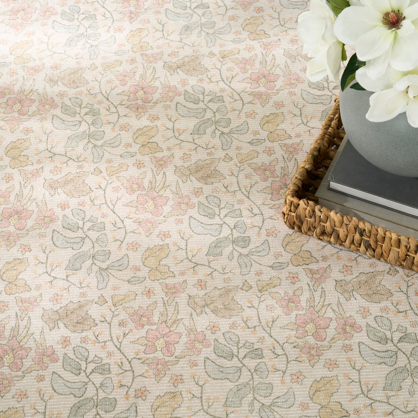Pastel floral rug in pink, peach and sage with a wicker tray holding a gray planter and white flowers.