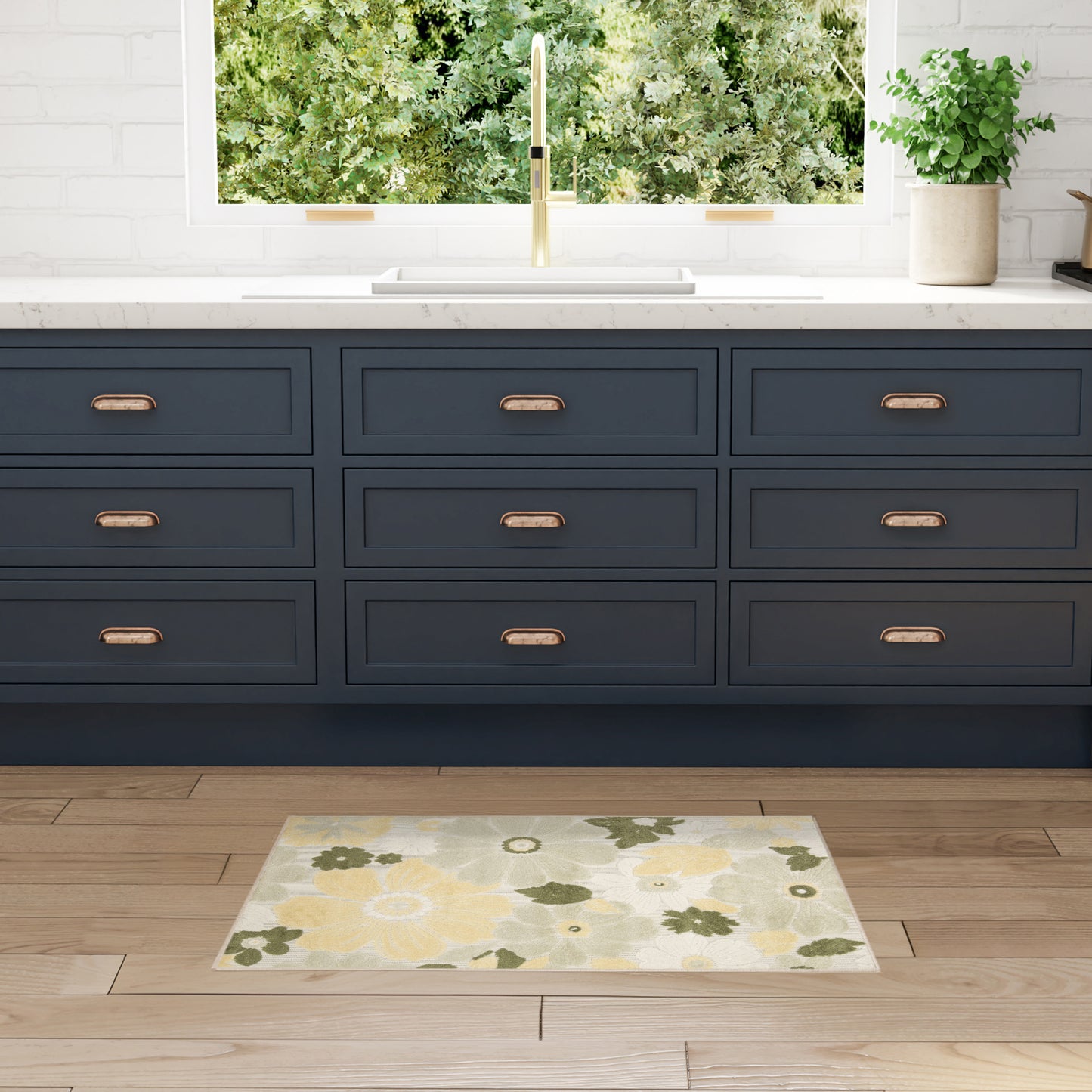 Navy blue cabinetry with copper handles, white countertop, gold faucet, window view of greenery, potted plant, yellow floral rug