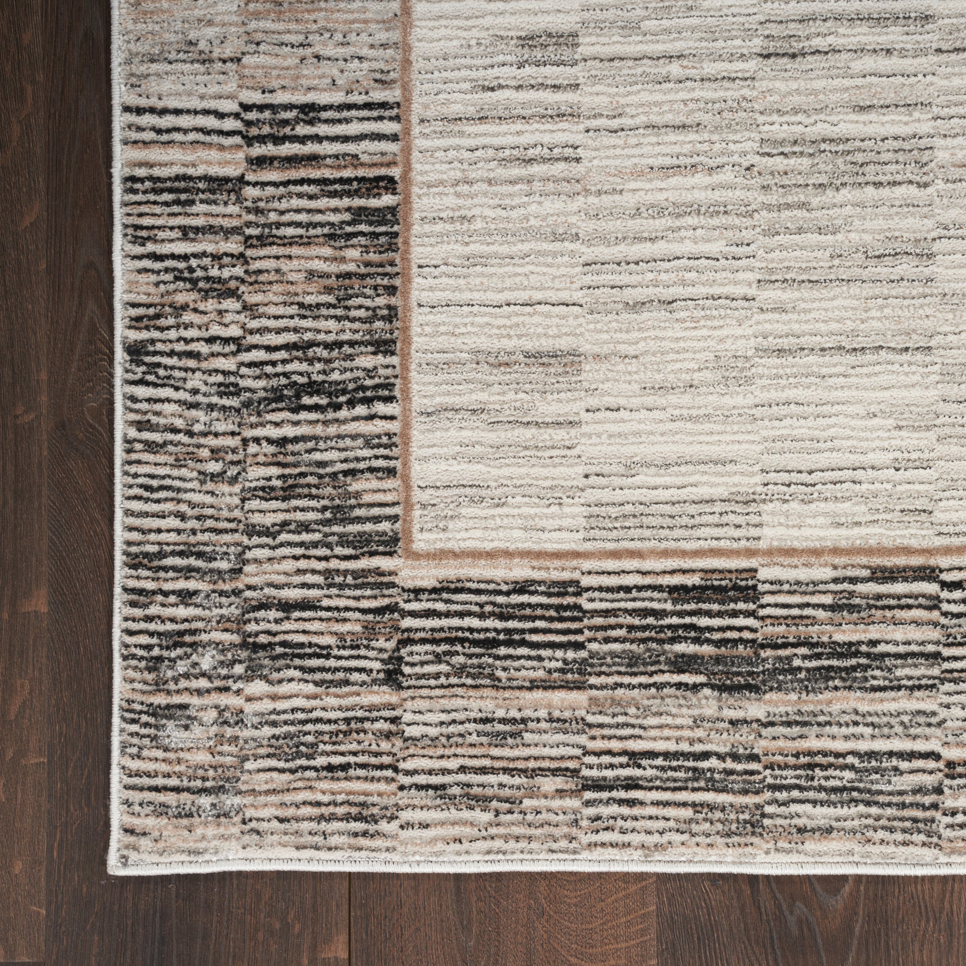 Neutral-toned rectangular rug with cream center and charcoal-brown striped border on dark hardwood floor.