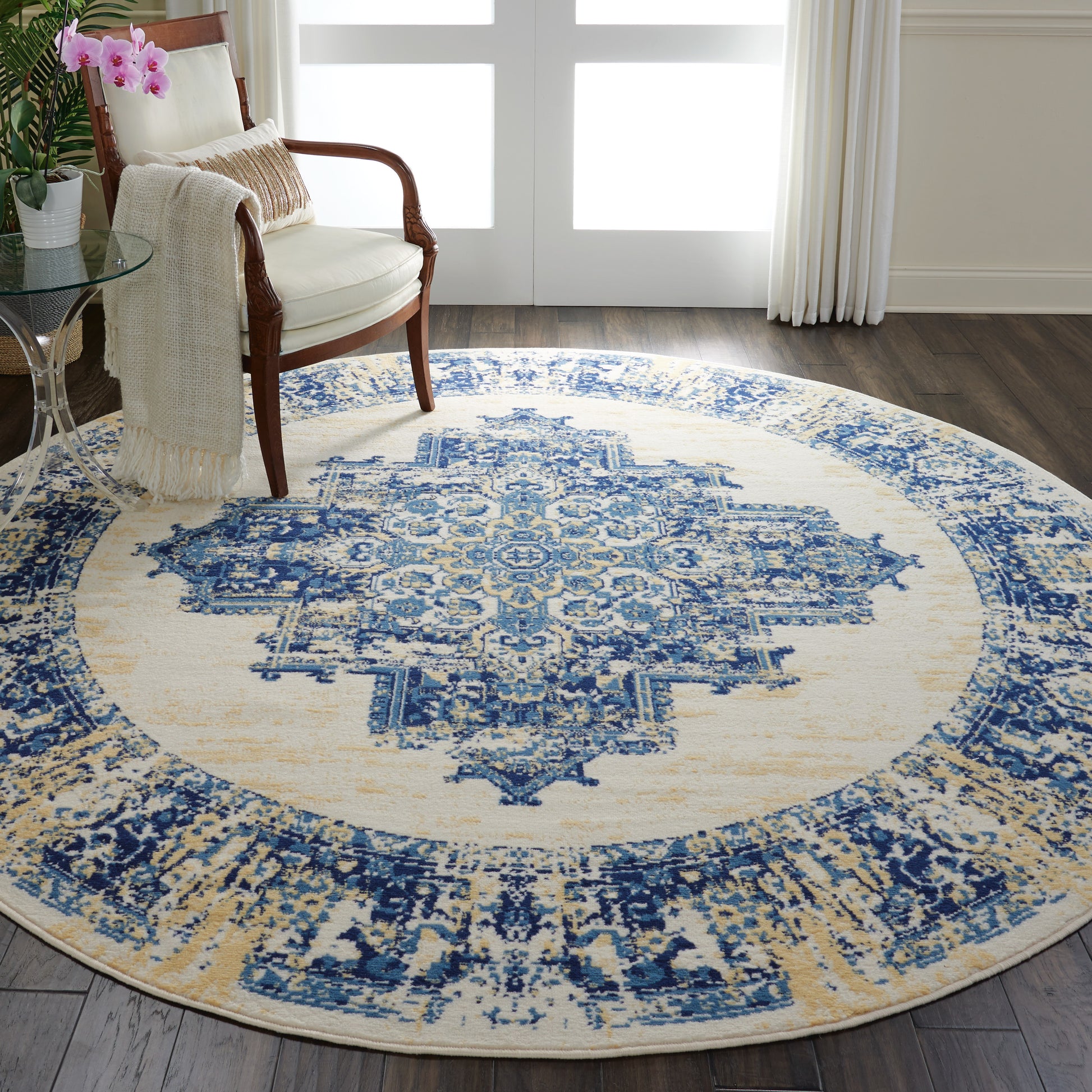 Round blue and ivory oriental rug with a central medallion in a living room beside a wooden armchair.