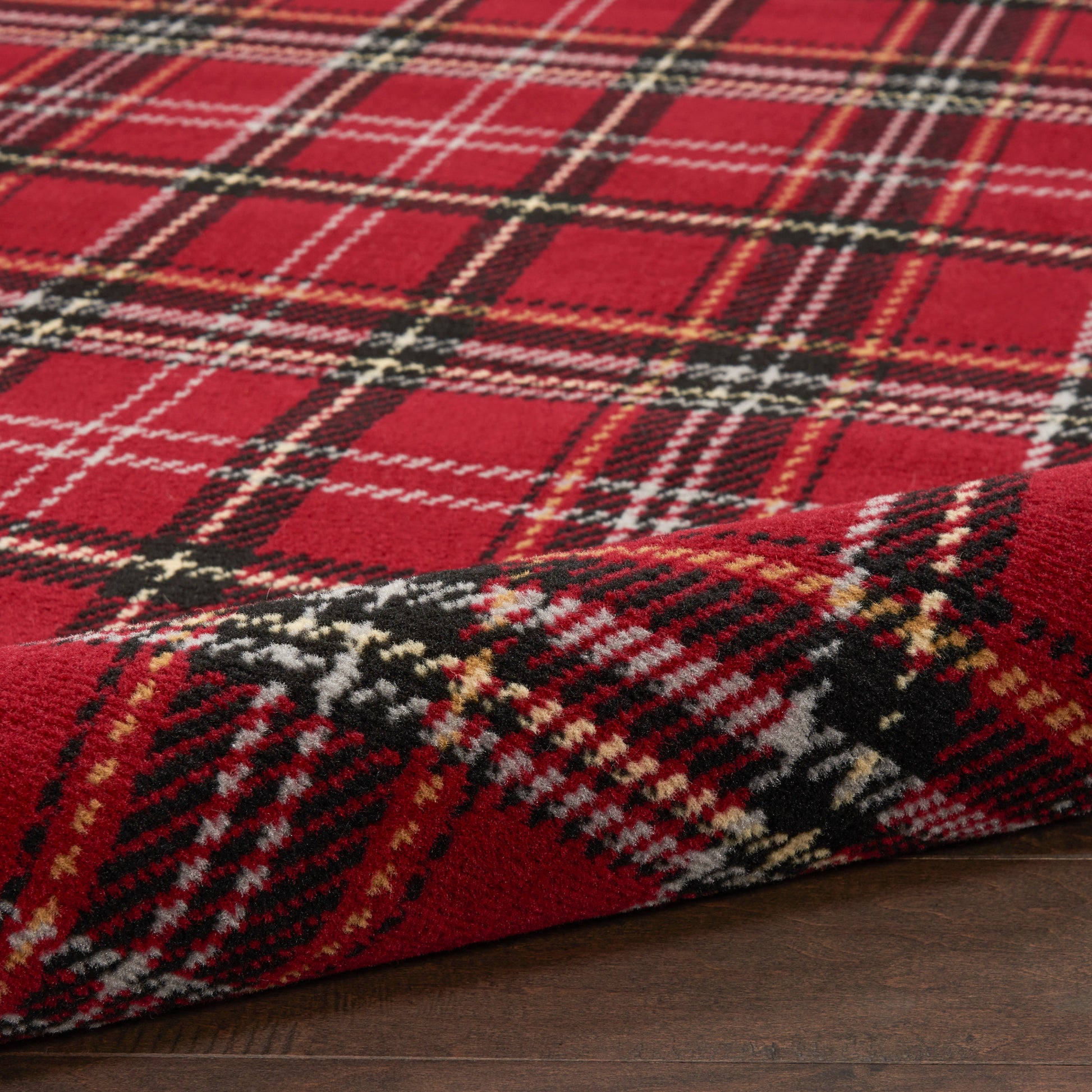 Red plaid wool rug with black, white and gold lines on a wooden floor.