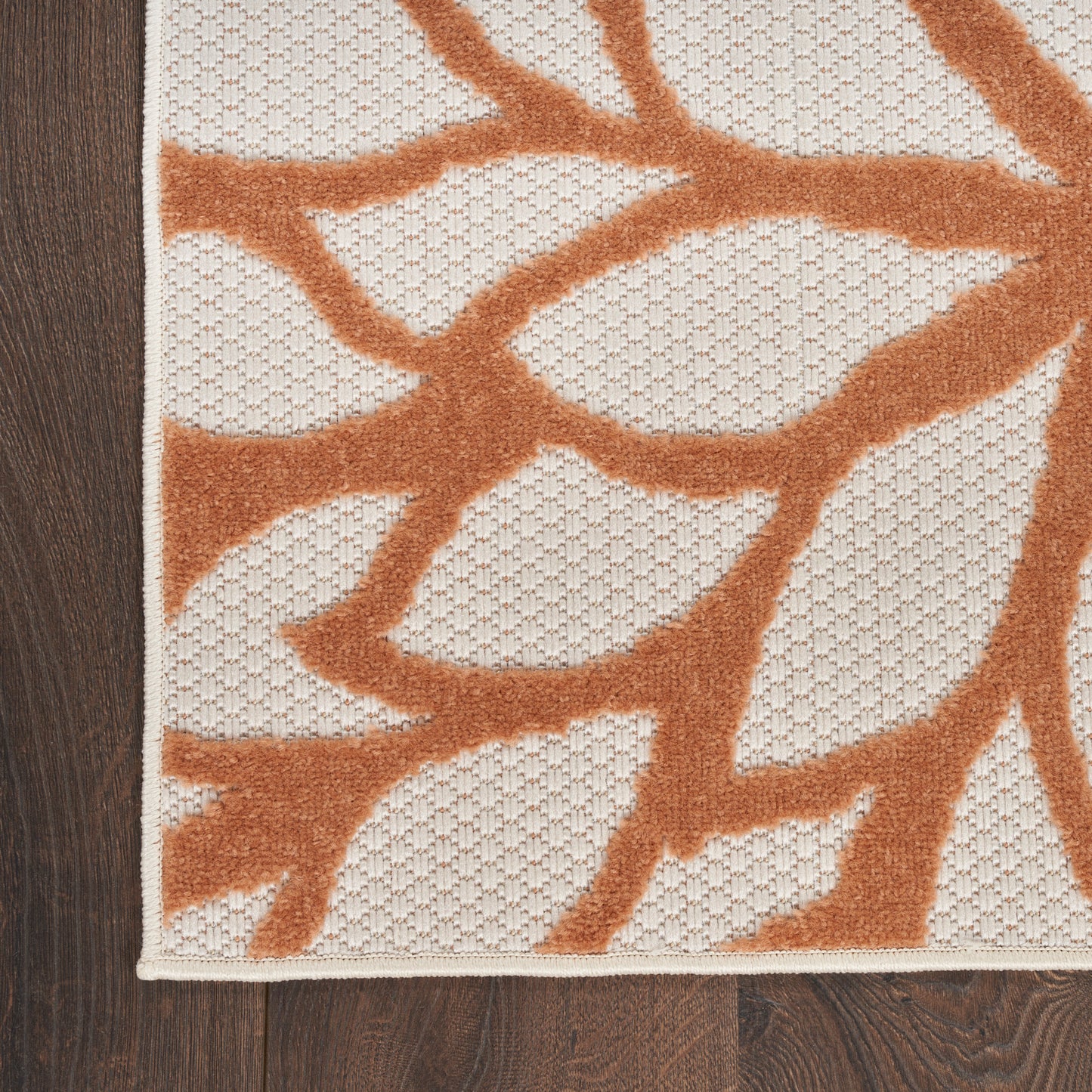 Cream outdoor rug with orange botanical vine pattern on dark wood floor, textured weave, 8' x 11'.
