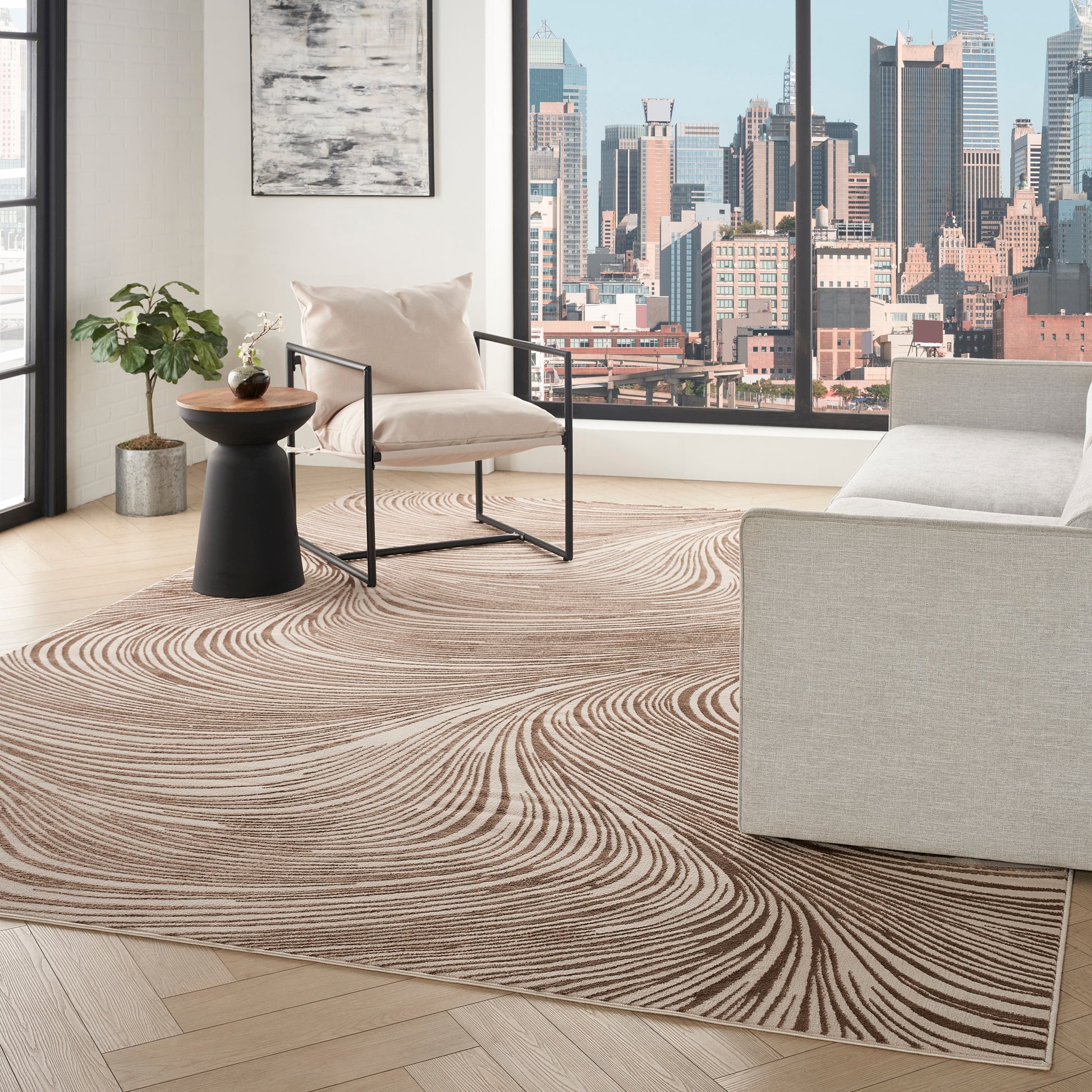 Living room with a beige-tan swirling area rug, light wood floor, modern cream sofa and armchair, city skyline window view.