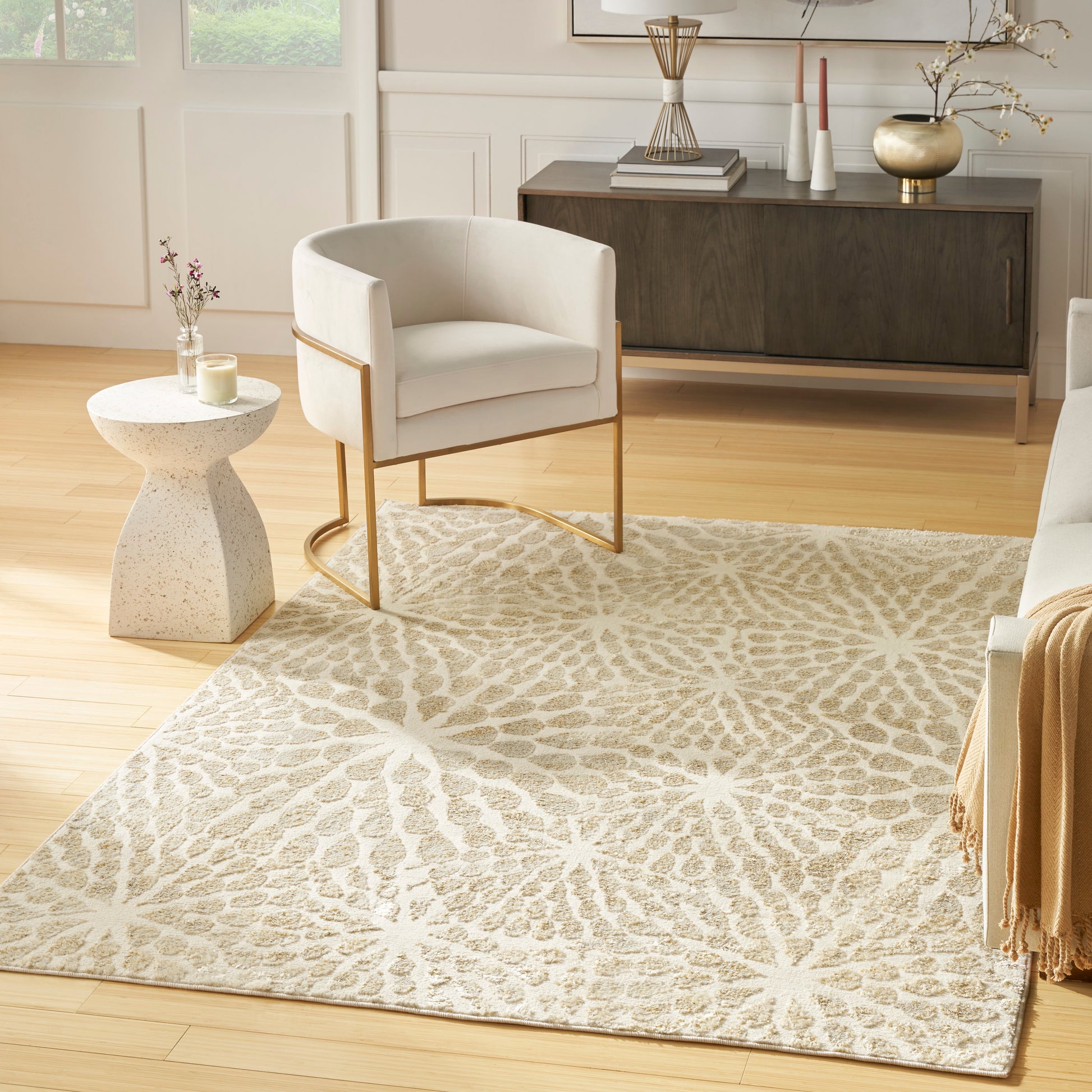 Cream armchair with gold metal legs, beige patterned area rug, concrete round side table in a bright living room.