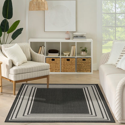 Neutral living room with beige armchair, white cubby console with wicker baskets, dark striped area rug, plants and framed art.