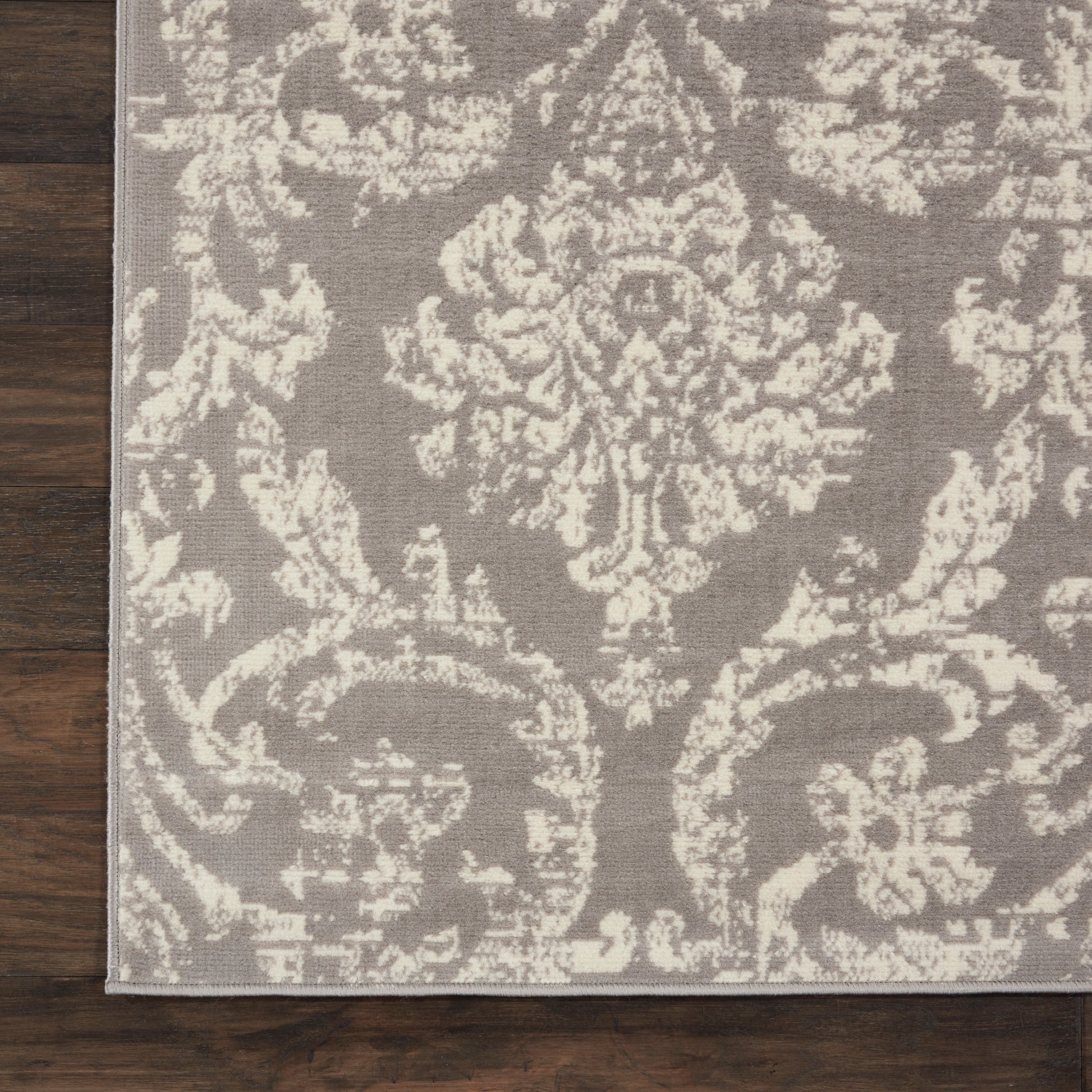 Rectangular taupe rug with cream damask pattern, woven texture, edge detail, laid on dark wooden floor.