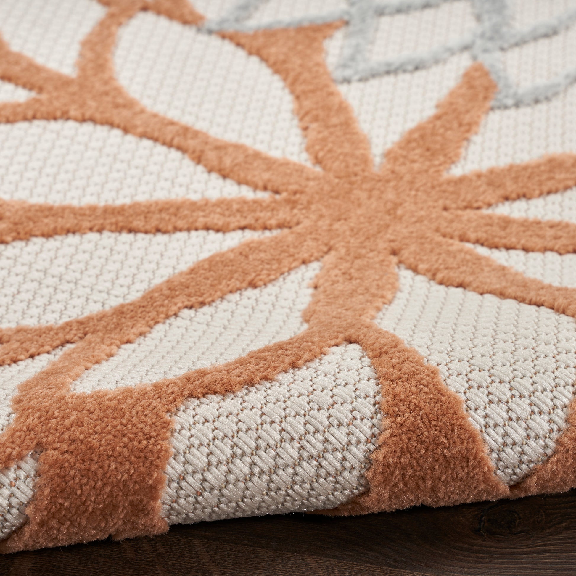 Close-up of a beige woven rug with an orange starburst floral pattern; textured loop pile and raised design.