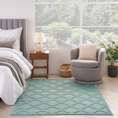 Bright bedroom with gray upholstered bed, white-gray bedding, wooden nightstand, lamp, round chair, beige pillow, teal rug.
