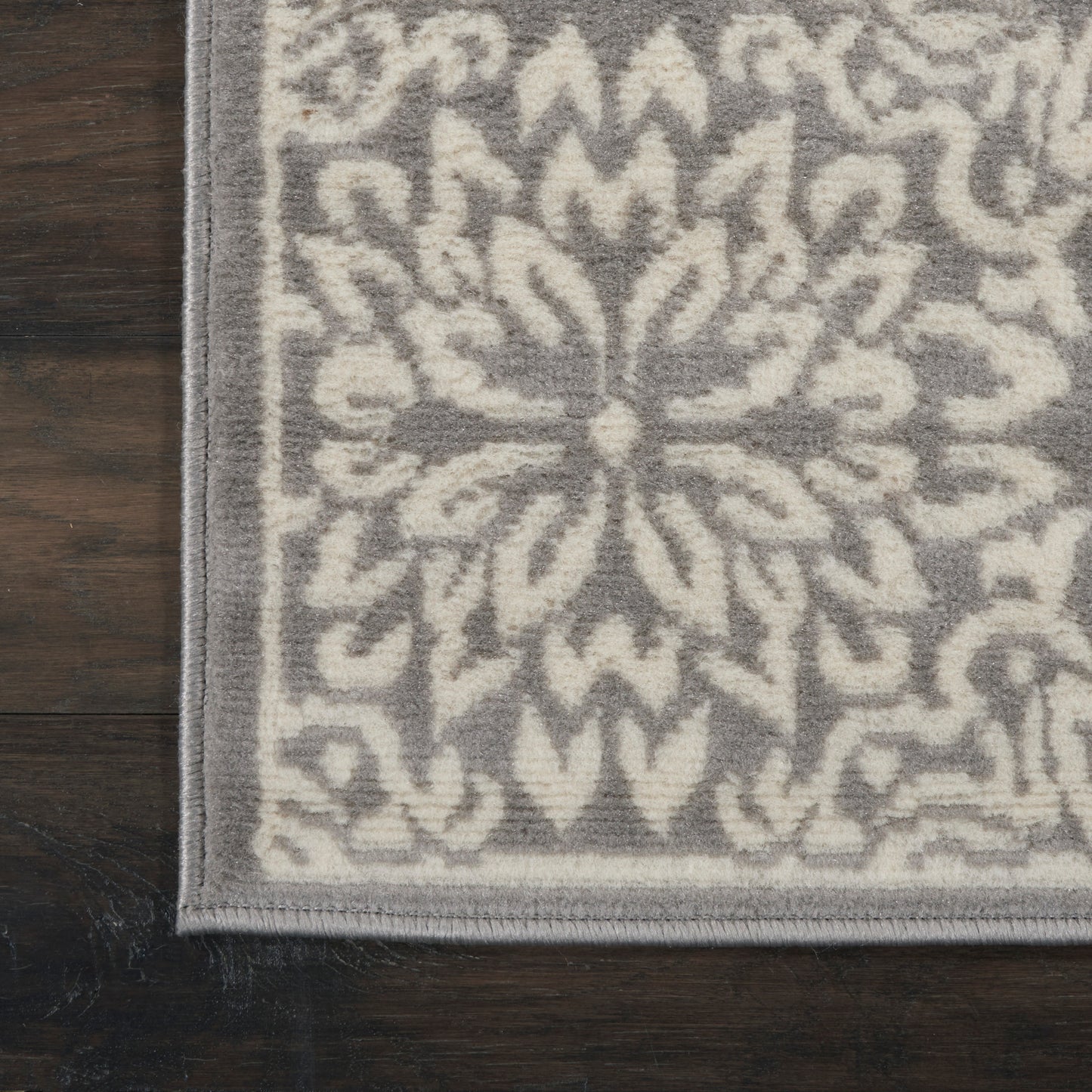 Gray rug with ivory geometric floral medallion pattern and border on dark wood floor.