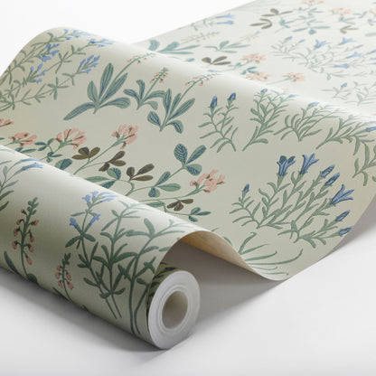 Beige botanical wallpaper with pastel blue, green, & pink herb-and-flower motifs, rolled up.