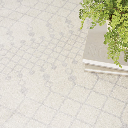 Beige rug with pale gray geometric lattice pattern; stack of books topped by a green fern.