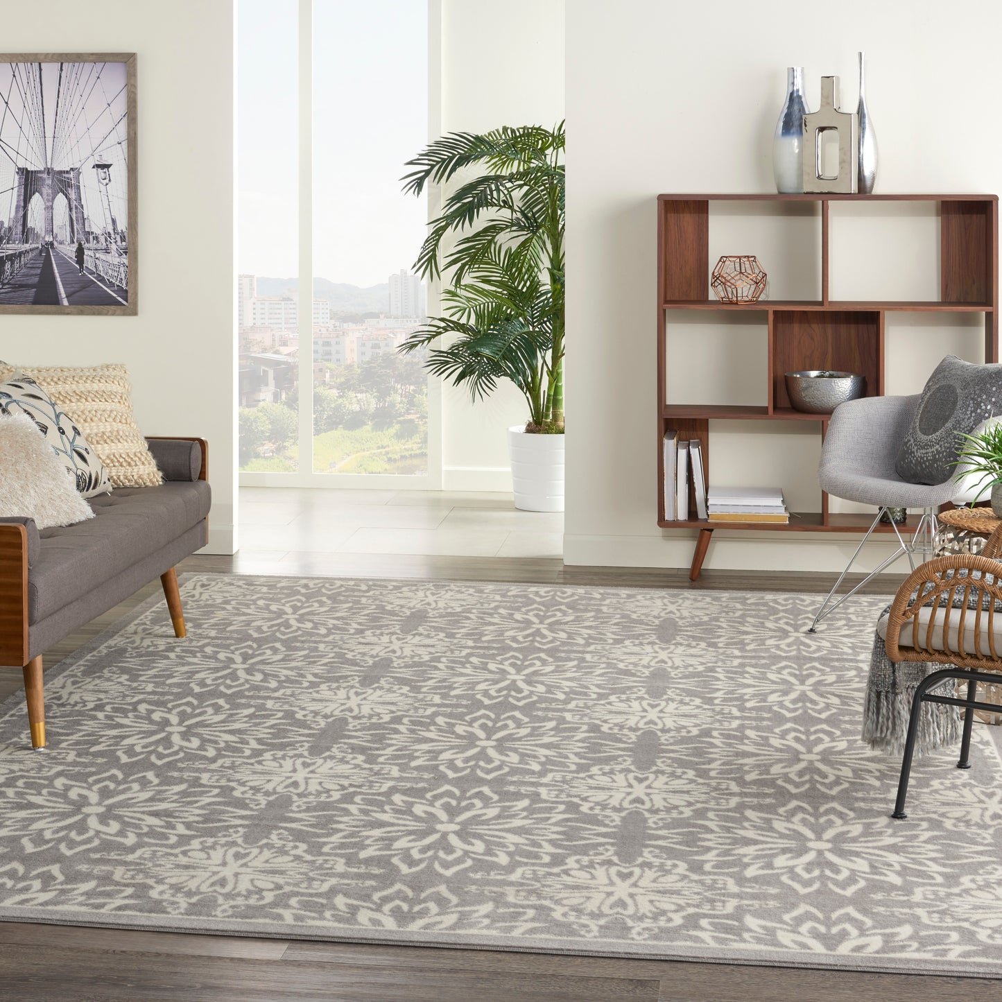 Modern living room with gray damask rug, sofa, wooden shelving, plant, and tall window with city view.