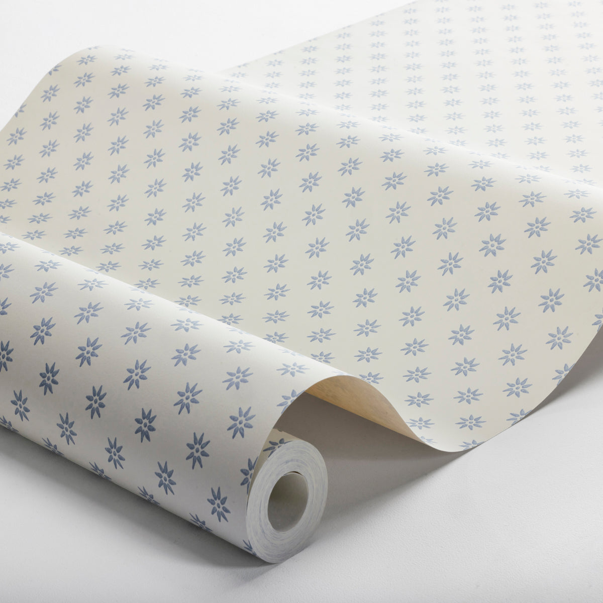 White wrapping paper with a fine blue snowflake pattern, rolled on a cardboard tube.