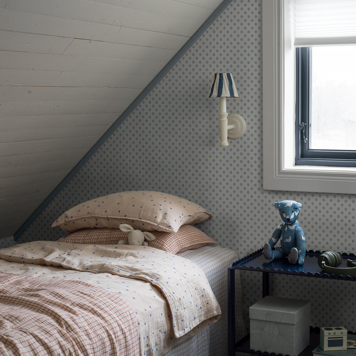 Single kid's bed in a blue polka-dot room with beige-pink patchwork bedding, bunny, blue striped wall lamp, blue side table.