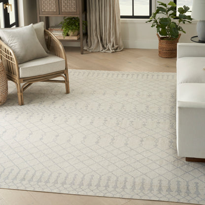 Neutral living room with light gray geometric patterned rug, rattan chair, beige cushions, wicker shelf, and potted plants.