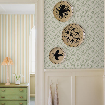 Vintage hallway vignette: green dresser with brass handles, striped and floral wallpaper, and three round wicker plates with black birds.