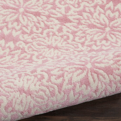 Pink rug with white floral/abstract pattern, soft pile texture, folded edge on dark wood surface.