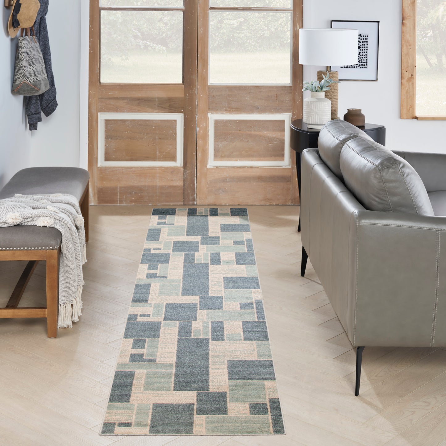 Geometric blue and beige rug runner on light wood floor in a modern living room with a gray sofa and wooden doors.