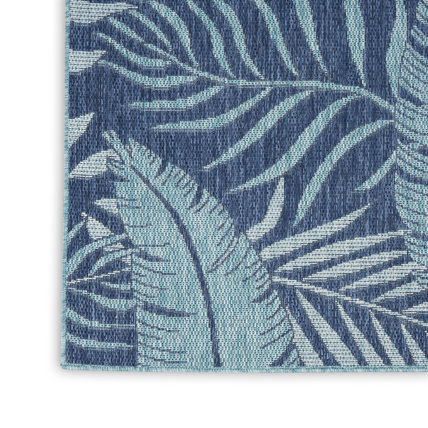Close-up of navy blue woven rug with teal tropical leaf pattern and light teal binding.