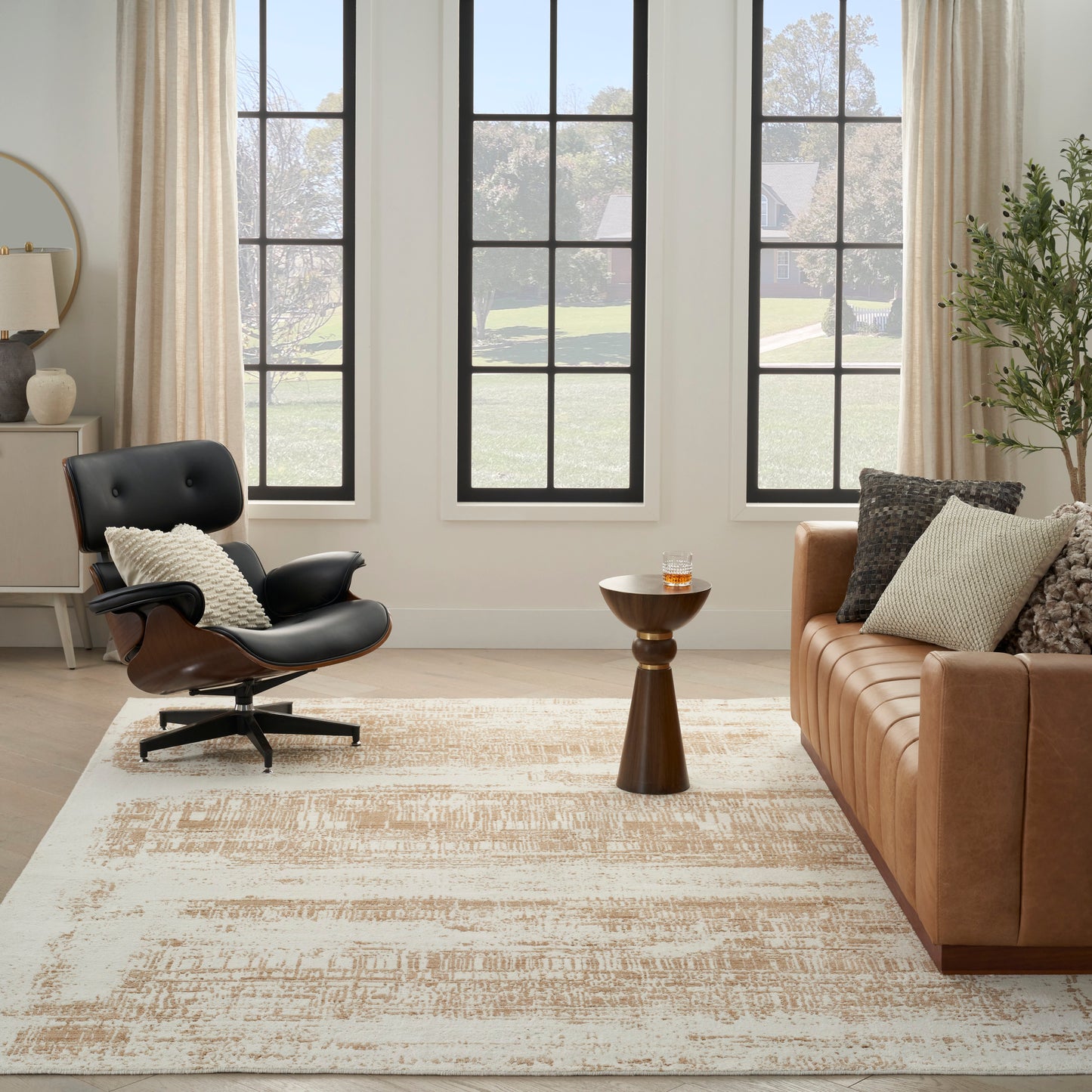 Living room with black leather lounge chair, tan sofa, wooden side table, beige rug, cushions, large grid windows.