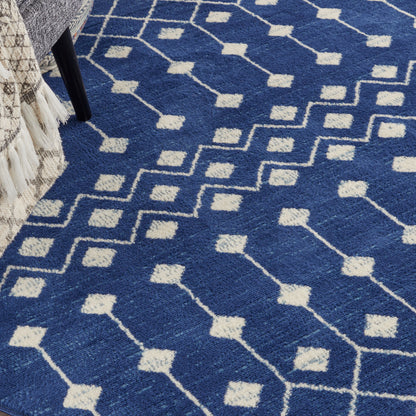 Blue rug with white geometric diamond lattice pattern; modern casual style, placed beside a bed.
