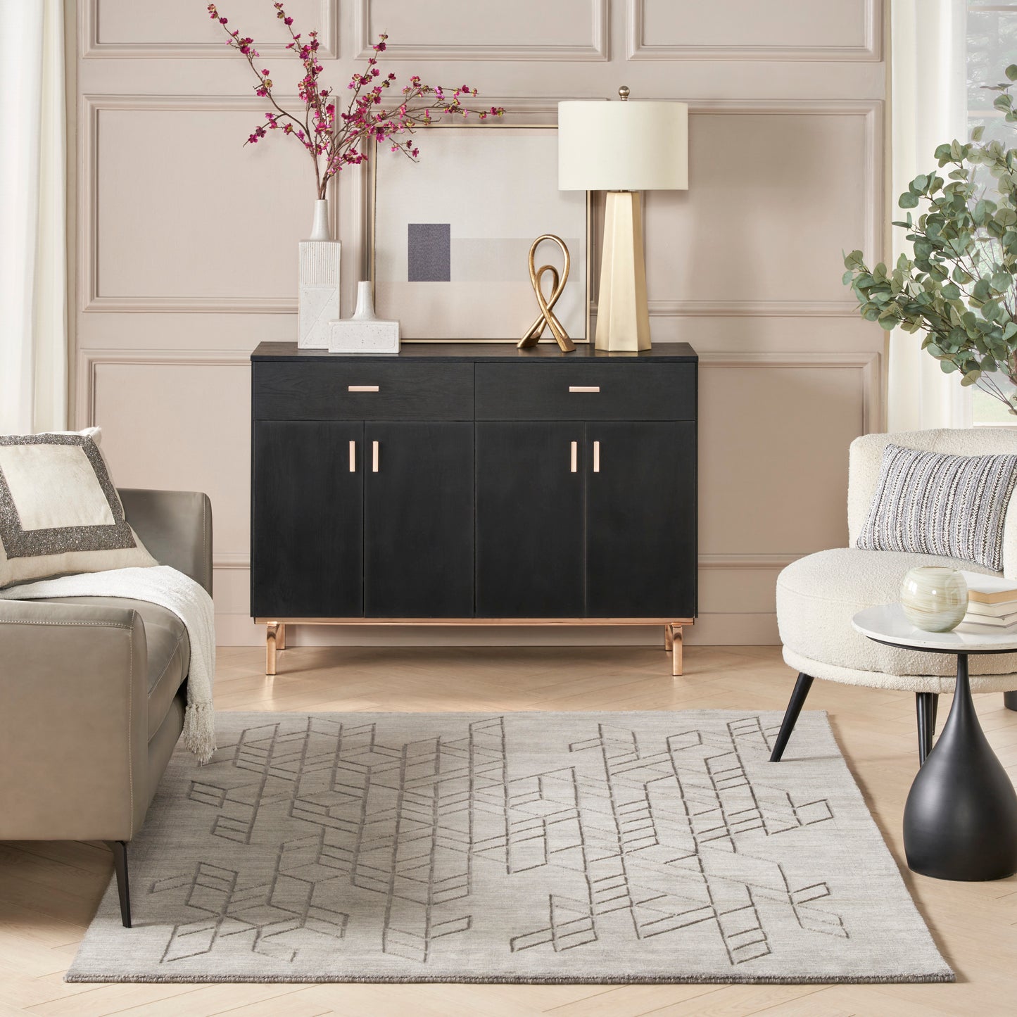 Black sideboard with gold legs and handles, topped with a lamp and decor, in a beige living room with a geometric rug.