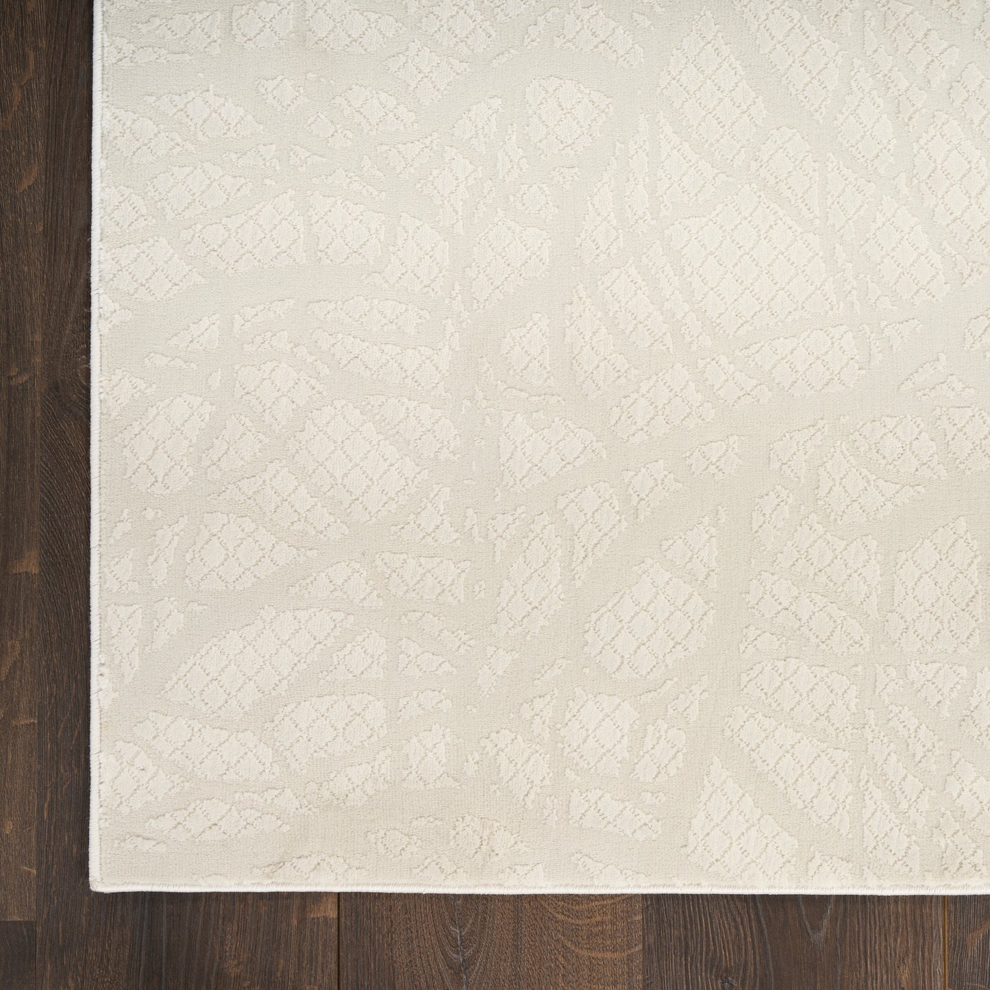 Cream textured area rug with subtle abstract geometric pattern on a dark wood floor.