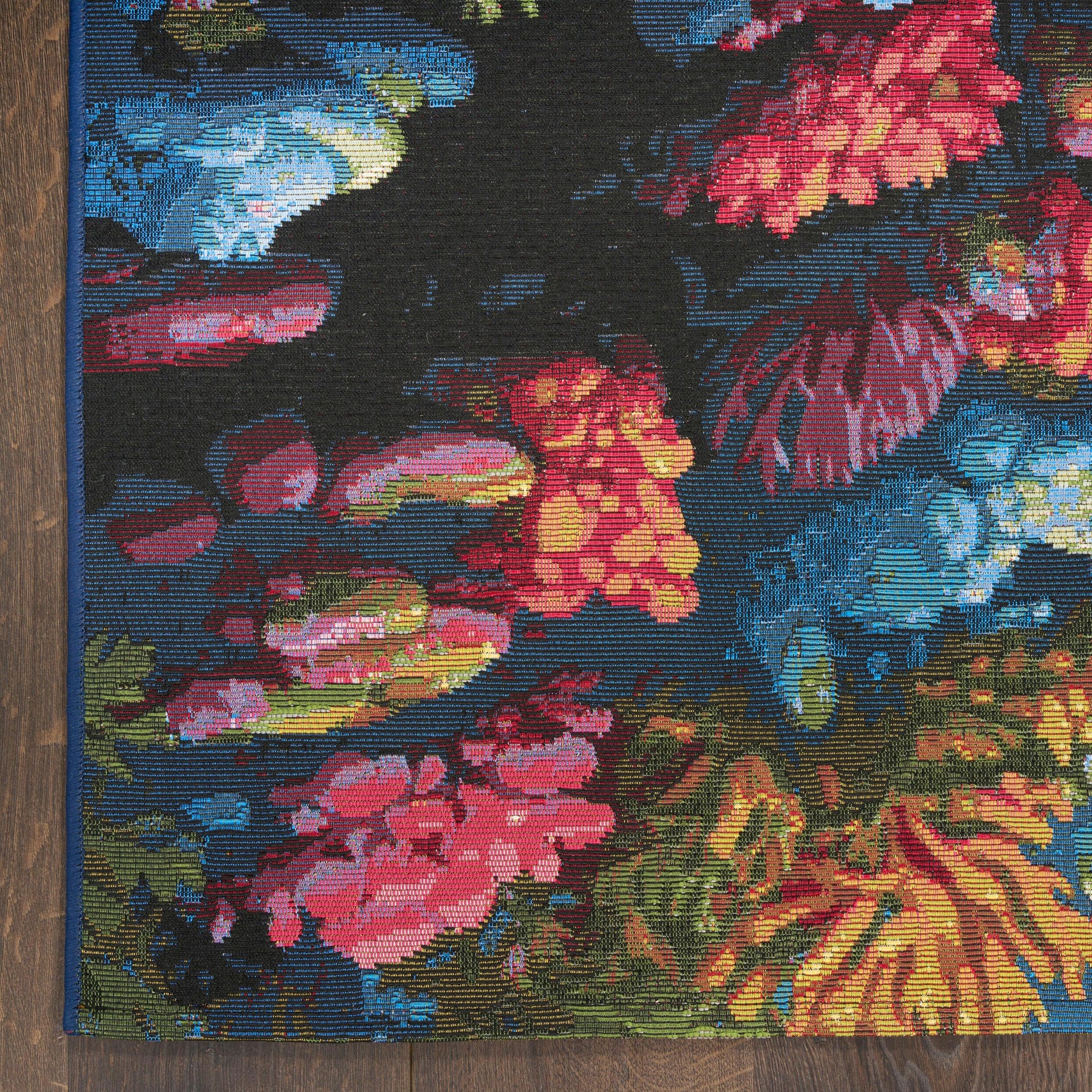 Colorful woven floral tapestry rug with blue edge trim, featuring pink, red and yellow blooms on a dark background.