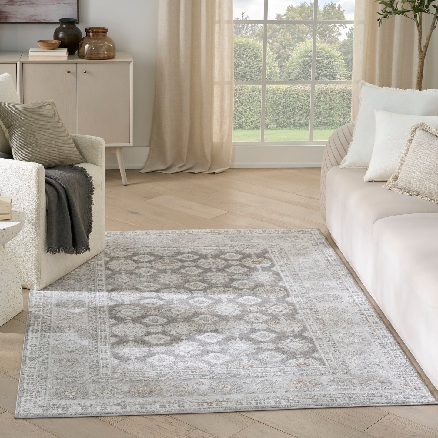Light grey and ivory patterned area rug with a distressed motif on a pale wood floor in a neutral living room.